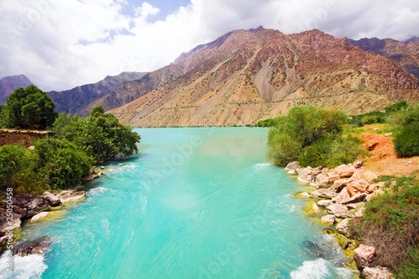 Fototapeta Mountanious moraine river and trees under cloudy sky