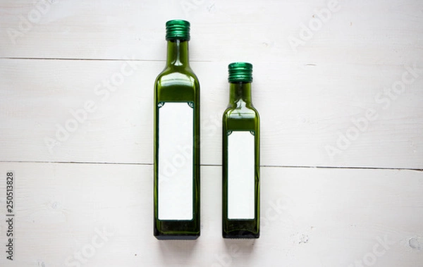 Fototapeta Green bottle for olive oil with white blank sticker for your teat of design. Flat lay, top view with white wooden rustic background. Mock up for product illustration.