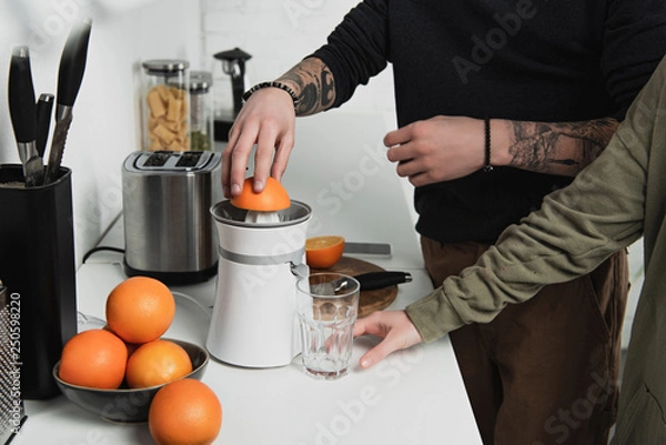 Fototapeta partial view of couple preparing orange juice during breakfast in kitchen