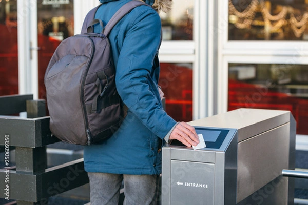 Obraz Close up outdoor rear portrait of unrecognizable man who comes up to the turnstile and puts the card to go inside/ using ticket to go through turnstile at station, tourniquet to the railway station.