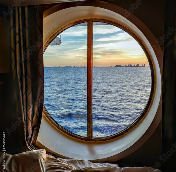 Fototapeta A view from the porthole window of a cruise ship, showing the city buildings in the sunset. The photo was taken inside a cabin on a Caribbean cruise.
