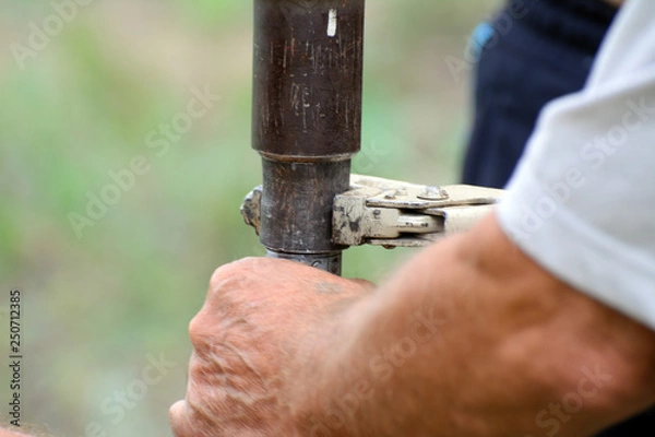 Obraz Male hands hold adjustable wrench wrapping the pipe.
