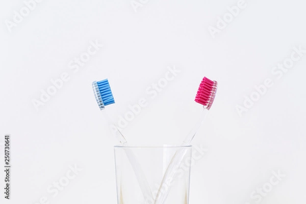 Fototapeta A glass with two plastic toothbrushes on white background. Love concept. Valentines day. Stomatology concept.