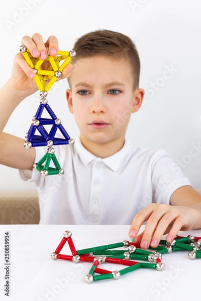 Fototapeta Close-up of child playing board game with magnetic sticks and balls while sitting at the table at home. Development, fine motor skills and creativity concept