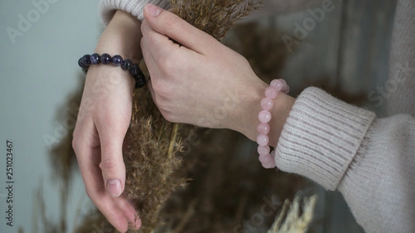 Fototapeta bracelets of purple and pink stones on the hand, in the hands of dried flowers, bracelets of amethyst and rose quartz