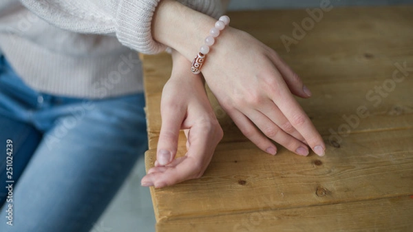 Obraz the girl on her arm has a bracelet made of pink stones (quartz), a bracelet made of quartz, hands, wooden table  (horizontally, light toned)