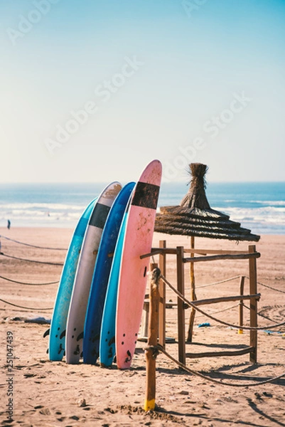 Fototapeta Different colors of surf on a the sandy beach in Casablanca - Morocco. Beautiful view on sandy beach and ocean. Surf boards for renting. Surfer school.