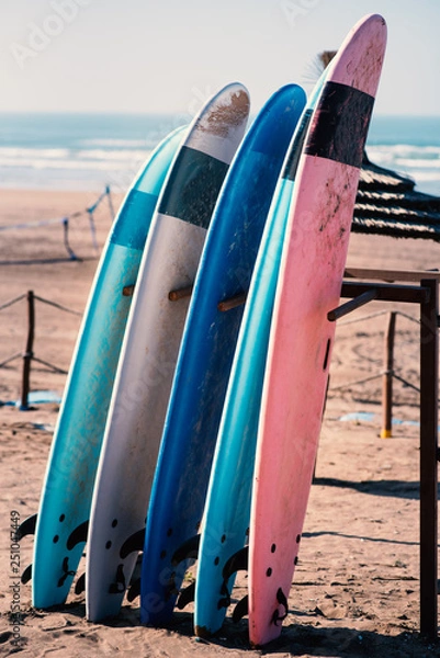 Fototapeta Different colors of surf on a the sandy beach in Casablanca - Morocco. Beautiful view on sandy beach and ocean. Surf boards for renting. Surfer school.