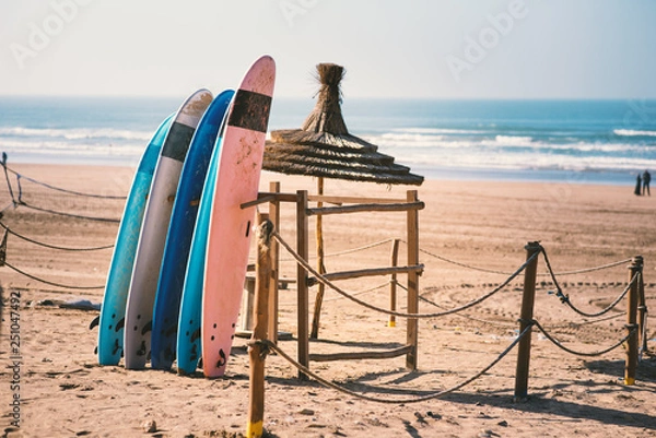 Fototapeta Different colors of surf on a the sandy beach in Casablanca - Morocco. Beautiful view on sandy beach and ocean. Surf boards for renting. Surfer school.