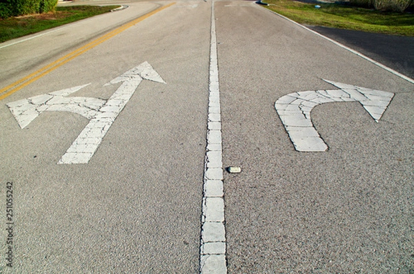 Obraz Looking down a stretch of empty road showing directional arrows painted on the road, pointing straight and left, and another pointing right, they are old and cracked.