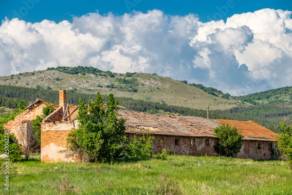 Fototapeta Abandoned agricultural buildings at the village of Rayanovtsi in Dragoman Municipality, Sofia Province, western Bulgaria, a karst mountain and beautiful cumulus clouds in the background