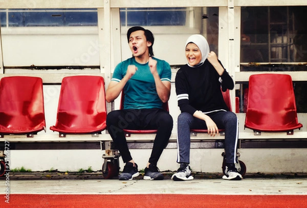 Obraz young couple sit in stadium with happy face expression, having fun and cheering to their team