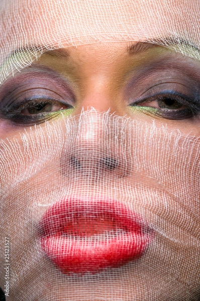 Fototapeta The woman's face with bright makeup veiled with gauze