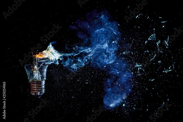 Fototapeta Сosmic explosion of burning light bulb with flying splinters of broken glass and smoke on isolate black background. Сoncept of creative art of starry sky, cosmos,  universe and the big bang theory.
