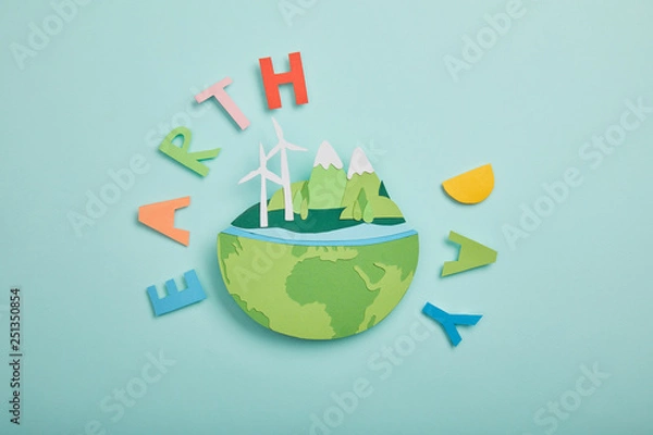 Fototapeta top view of paper cut planet with renewable energy sources and colorful paper letters on turquoise background, earth day concept