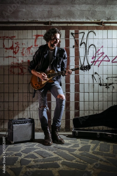 Obraz A street musician playing on guitar in the underpass. Vagrant lifestyle. Playing in the underpass to make a living. Unemployed musician. Future rock star.
