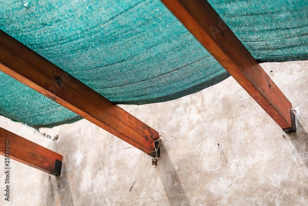 Fototapeta A plastic sun protection mesh on wooden beams and a cracked concrete wall