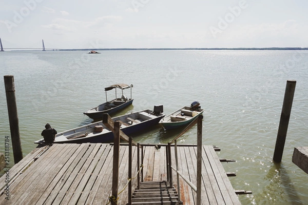 Fototapeta A man tie a rope to secure his boat to a wooden jetty. view from a wooden jetty