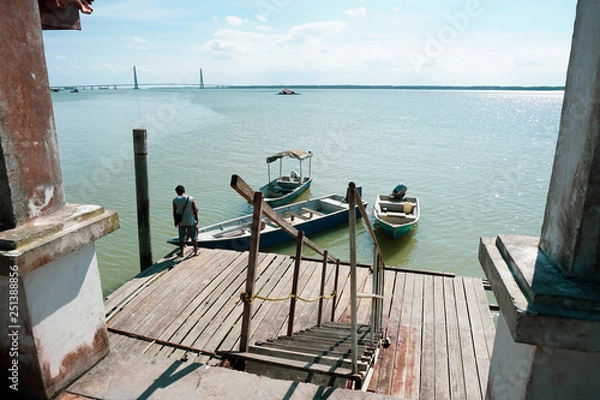 Fototapeta View of a man by the jetty securing rope from his boat to a wooden jetty. view from a wooden jetty