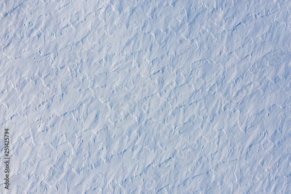 Fototapeta Snow covered land texture with grunge surface created by windy weather. Abstract winter backdrop in blue tones, top view from drone