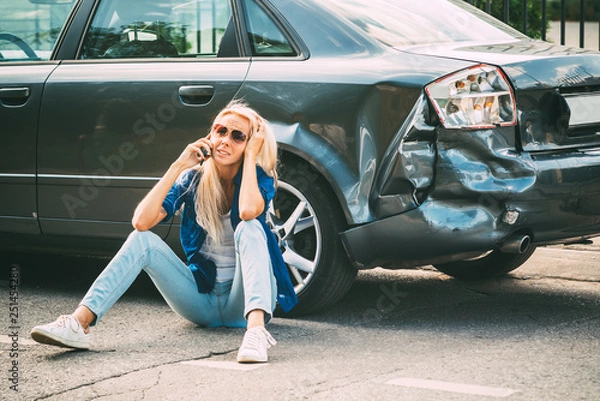 Fototapeta girl sits on the road, near the broken car and calls on the phone, calling for help.