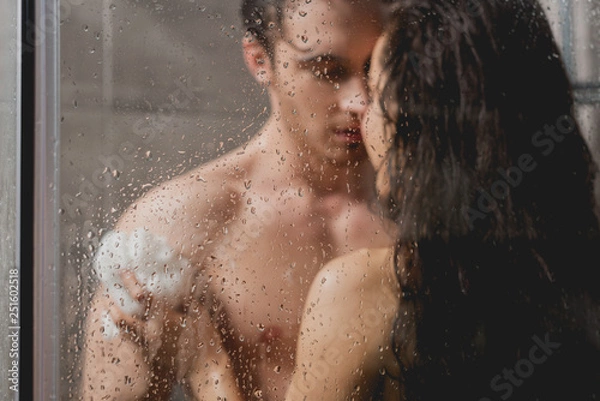 Fototapeta selective focus of man and beautiful woman hugging and taking shower with loofah in cabin
