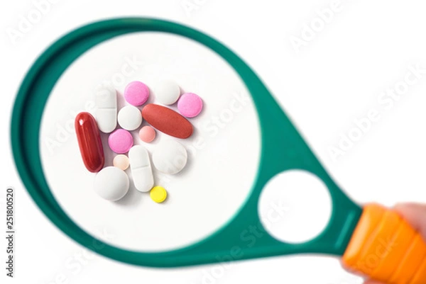 Fototapeta pills under a magnifying glass on the white background. Testing, verification and determining pharmaceutical counterfeiting or fake
