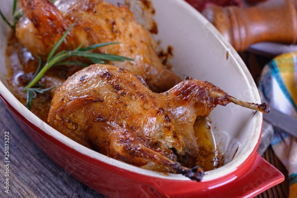 Fototapeta Delicious baked quails in a ceramic roasting pan on a wooden table prepared for a delicious lunch or dinner