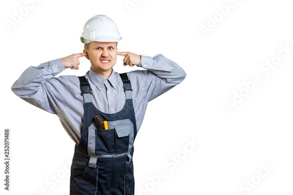 Fototapeta The builder in overalls and a protective helmet covers his ears with his hands. It is unbearable to hear the opinion of the customer about the work done. Isolated.