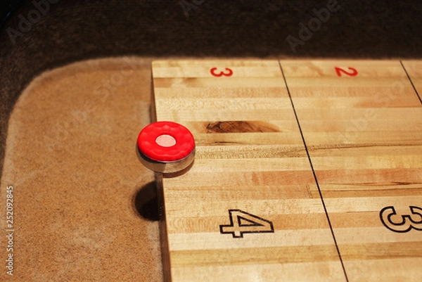 Fototapeta red shuffleboard disc on the table at five point mark. Shuffleboard game in progress, night, interior.