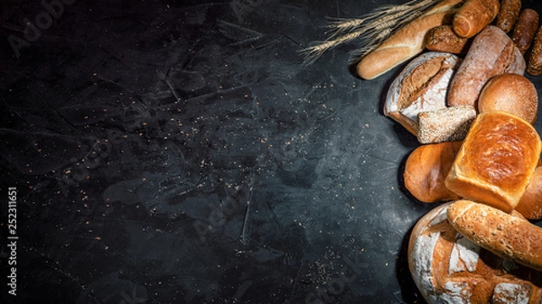 Fototapeta Assortment of fresh baked bread on dark background. White and rye bread, buns with copy place