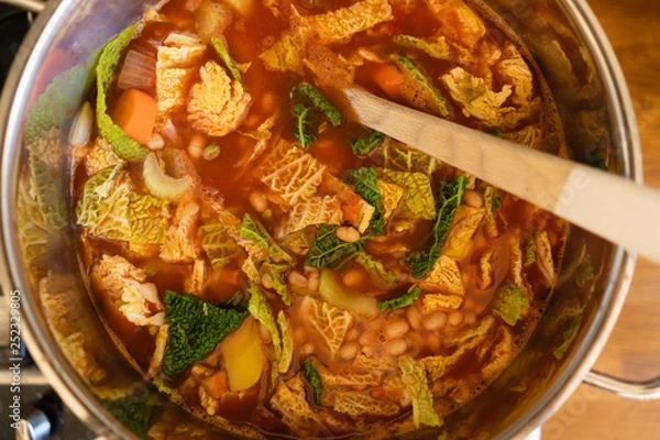 Fototapeta Pot with homemade Minestrone soup, a traditional Italian one pot dish made of tomatoes, carrots, onions, savoy cabbage, cannellini beans, celery and potatoes for a healthy vegetarian low carb diet