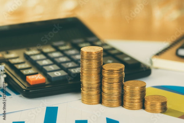 Obraz Coin stack and financial graph paper sheet with calculator on working table, business planning vision and finance analysis concept.