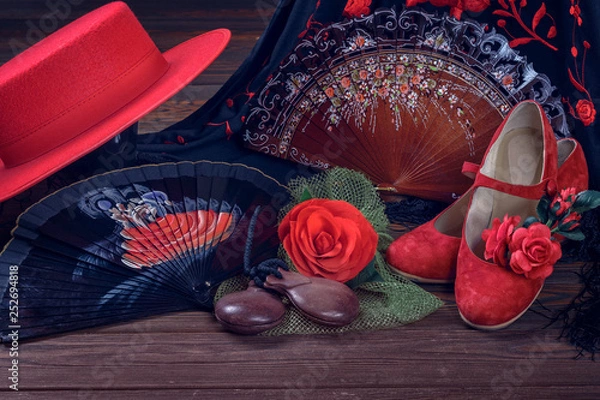 Fototapeta Beautiful and bright accessories for flamenco dance on a wooden background in a low key. Shawl, hat, fan, shoes, castanets and a flower for the hair.