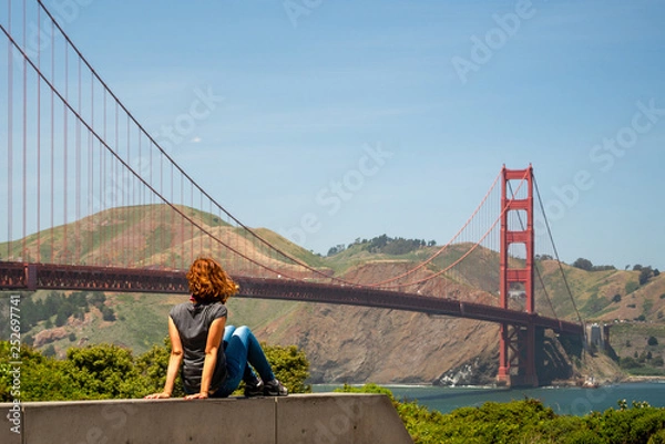 Fototapeta Young woman is watching Golden Gate bridge from a tourist point near the bridge in San Francisco, United States of America