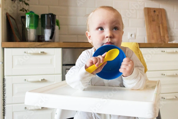 Obraz baby eat from blue plates with a yellow spoon