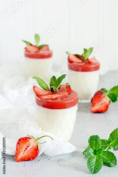 Fototapeta Italian dessert Panakota with strawberry coolies, fresh berries and mint on a white background with hard shadows. Creamy milk tender dessert in a glass. Close up. Vertical shot. Summer dessert. 