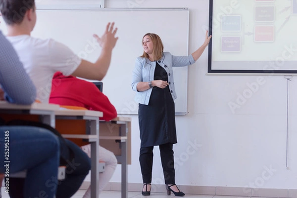 Obraz Female professor explain to students and interact with them in the classroom.Helping a students during class. University student being helped by female lecturer during class.