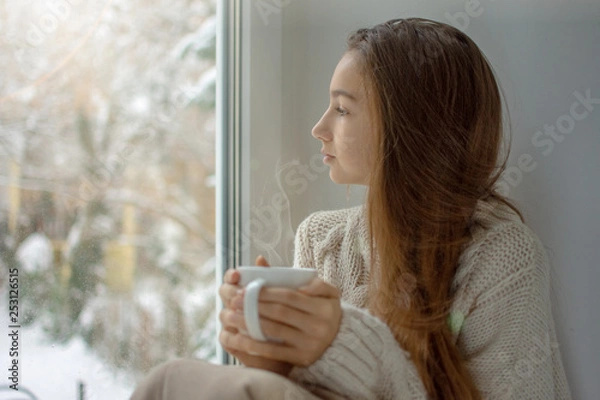 Obraz Young woman looking through window enjoys drinking coffee