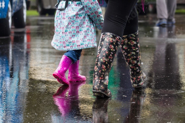 Fototapeta Dewsbury / Great Britain - May 2, 2016:  Legs of mother and child walking though the rain with wellies and rain boots on.  Reflections can be seen on the wet road pavement.