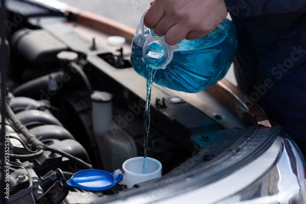 Obraz Man is holding bottle of blue antifreeze in hands and pouring antifreeze liquid for washing car screen