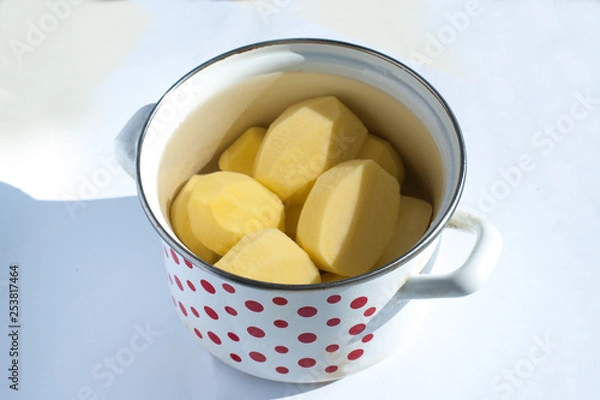 Fototapeta peeled raw potatoes in a pot on a white background
