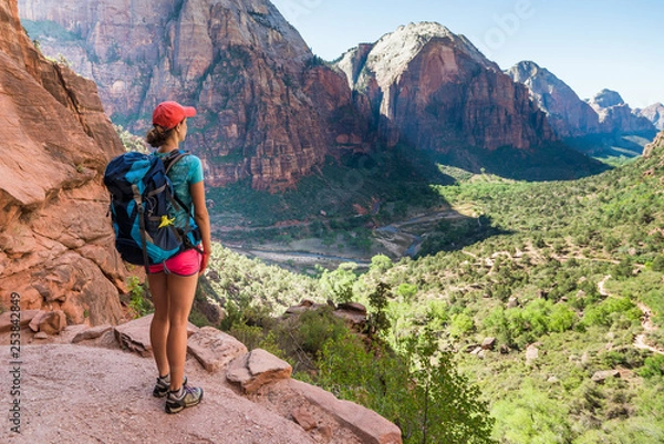 Fototapeta Young woman wearing backpack is looking at the view on the trail to Angel's Landing in Zion National park in Utah, USA. Female on a hiking trail in Zion National Park in Usa.
