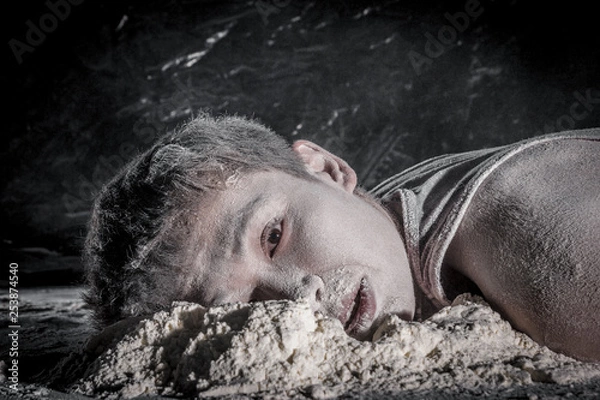 Fototapeta alienated vietnamese guy lying on floor with soiled face in white powder on black background. concept of absolute hopelessness of indifference and human hopelessness.  toned in sepia color, instagram