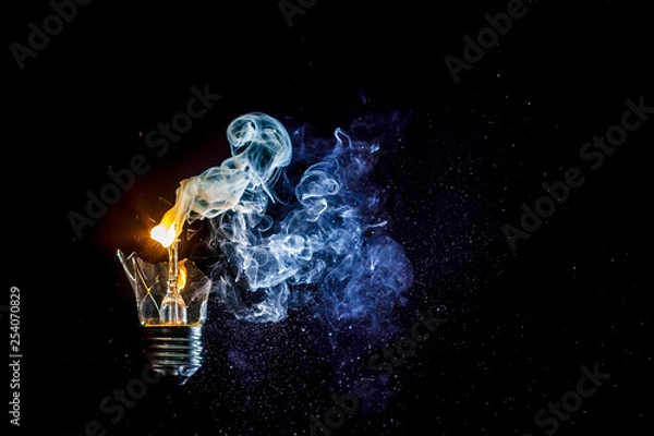 Obraz Сosmic explosion of burning light bulb with flying splinters of broken glass and smoke on isolate black background. Сoncept of creative art of starry sky, cosmos,  universe and the big bang theory.