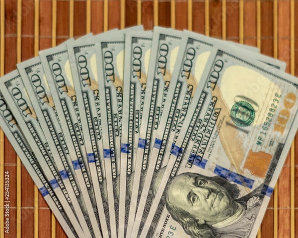 Obraz The stack is 100 dollar bills USD spread out like a fan, on a wooden background.