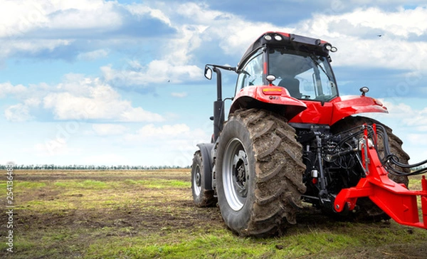 Obraz Tractor working in a field against a cloudy sky