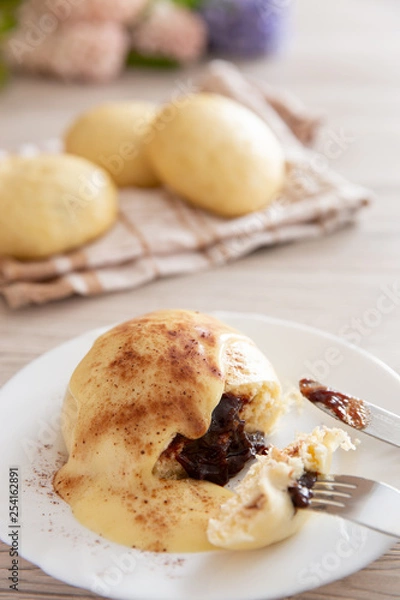 Fototapeta Germknödel oder Hefeklöße mit Pflaumenmusfüllung und Vanillesoße auf weißem Teller und hellem Holzuntergrund