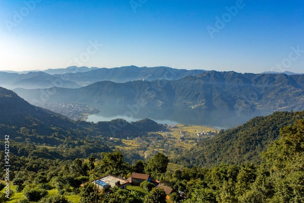 Fototapeta house on a hill against the background of the city of Pokhara in a mountain foggy morning valley with Phewa lake under a clear blue sky