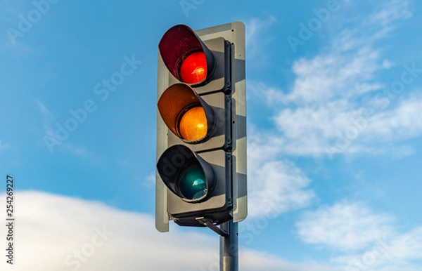 Fototapeta An English traffic light sits isolated against a bright blue sky with the red, orange and green lights